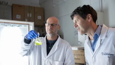 Professors Mark Moore and Tom Bibby examine a laboratory flask containing green algae culture.