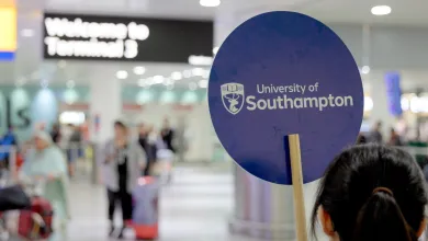 A UoS ambassador waits to greet international students at an airport terminal. She holds a sign bearing our crest and reading "University of Southampton"