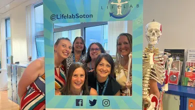 The LifeLab team poses in a blue photo frame at the LifeLab Showcase, with a skeleton model nearby.