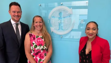 Stephen Morgan, Kath Woods-Townsend and Satvir Kaur gather in front of the LifeLab logo on a bright light blue wall.