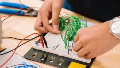 Hands connecting wires and components on a breadboard for electrical testing and prototyping