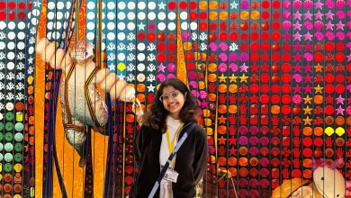 Design Management student smiling in front of a colourful textile and craft exhibition display.