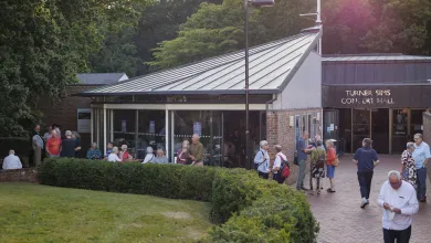 The Turner Sims Concert Hall building with groups of people dotted around the entrance. Some groups sit at tables enjoying a drink in front of a hedged grassy area.