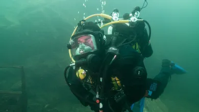 Commercial diver in full-face diving equipment and blue fins underwater during a dive.