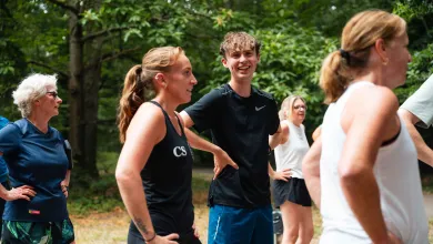 Several people in sportswear stand on a woodland path at the end of a group running session. There are trees and greenery in the background.