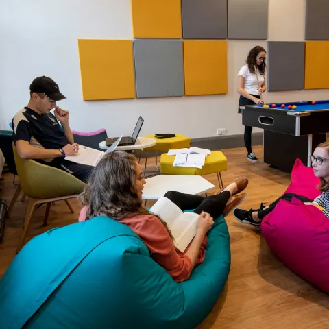 Group of students in common room, sat talking and playing pool.