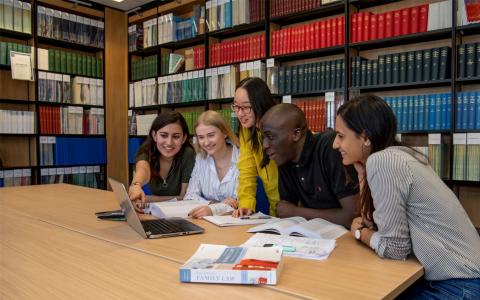 Students huddle around laptop in the library law collection
