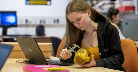 An archaeology student examines an object at a table, using a measuring device