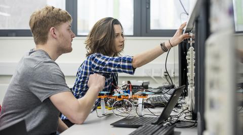 Two students working on the electronics of a small drone, at a workbench in the teaching lab.