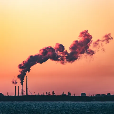 A shot of an industrial shoreline silhouetted at sunset, with smoke from a refinery curling into the sky.