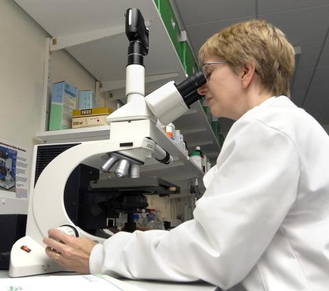 Person in lab coat using light microscope with digital camera attachment
