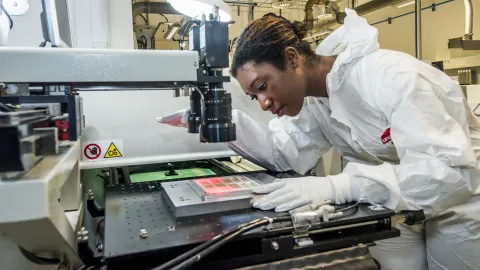 A student wearing protective clothing uses printed electronics and materials equipment