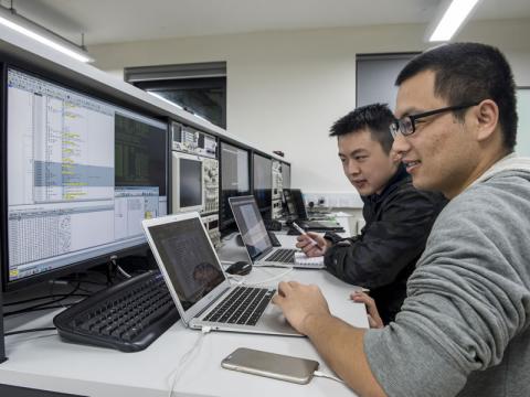Two cyber security researchers work at a bank of computer screens