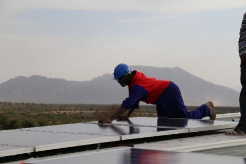 person wearing construction clothing fitting solar panels for renewable energy on roof in kenya