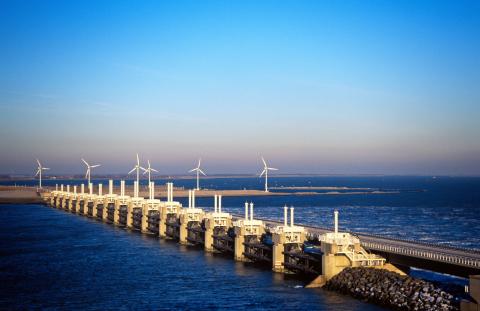A wide shot of a storm surge barrier, with several wind turbines spinning in the background.