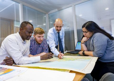 A Southampton Geospatial researcher points to a map as he stands over colleagues from the team