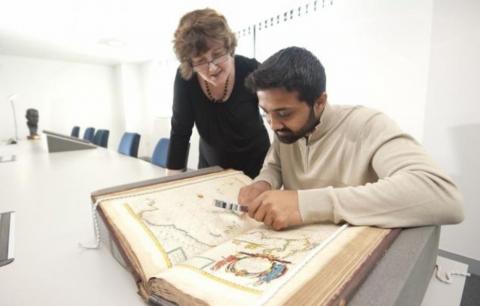 An archaeology student closely examines an historical text while a lecturer looks over his shoulder