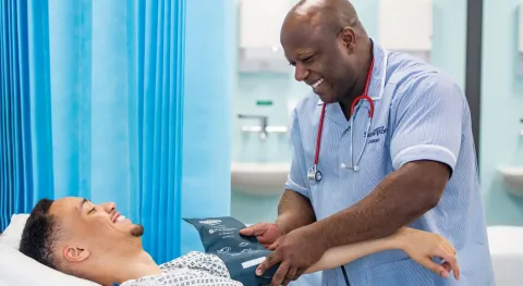 A patient and Southampton student nurse smiling at each other in a hospital room, as the nurse takes the patient's blood pressure.