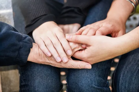 A close up of several overlapping hands holding each other, representing young, mid-life and older generations.