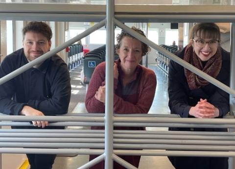 Three arts and humanities academics smile for the camera from behind metal bars