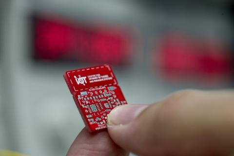 Extreme close up of a red internet of things circuit board held between finger and thumb