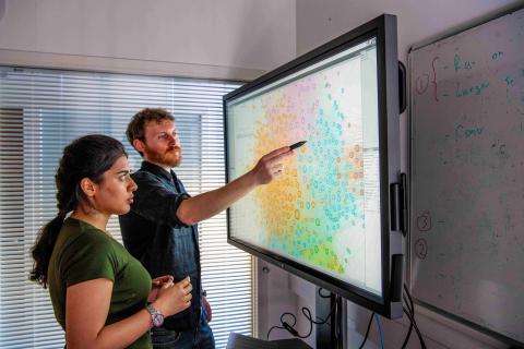 Two researchers looking at a multi-coloured plot on a large interactive screen