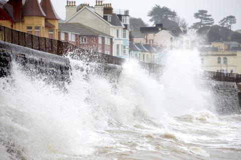Waves crashing on a sea wall opposite houses 