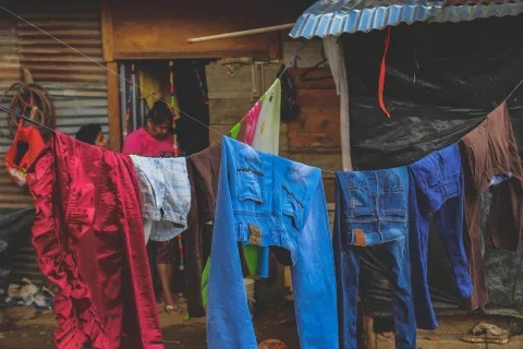 Woman walking past numerous people sitting along a fence covered in laundry