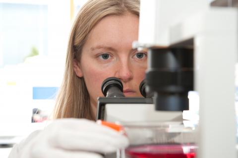 face of a woman placing a sample under a microscope