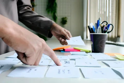 A finger points to a series of cards, another hand in the background gesticulates