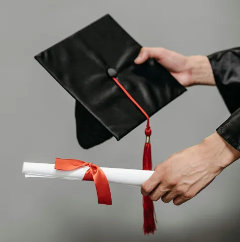 Hands proffer a graduation cap and scroll