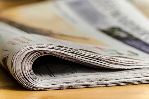A rolled-up newspaper on a wooden surface, with visible pages and text.