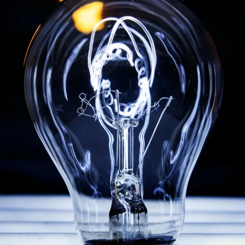 lose-up of an illuminated incandescent light bulb with visible filaments against a dark background.