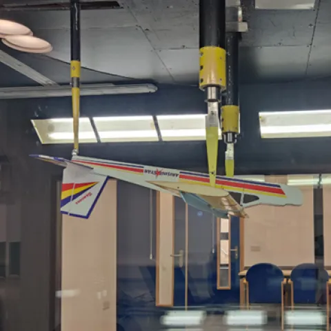 An upside‑down model aeroplane with colourful stripes is suspended from the ceiling inside a wind tunnel at the University of Southampton.