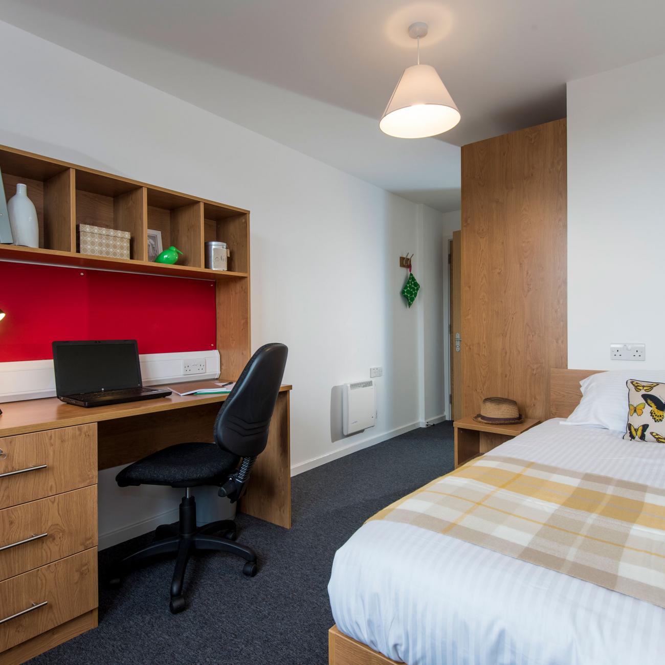 A modern student bedroom with white walls, wooden desk and neatly made double bed.
