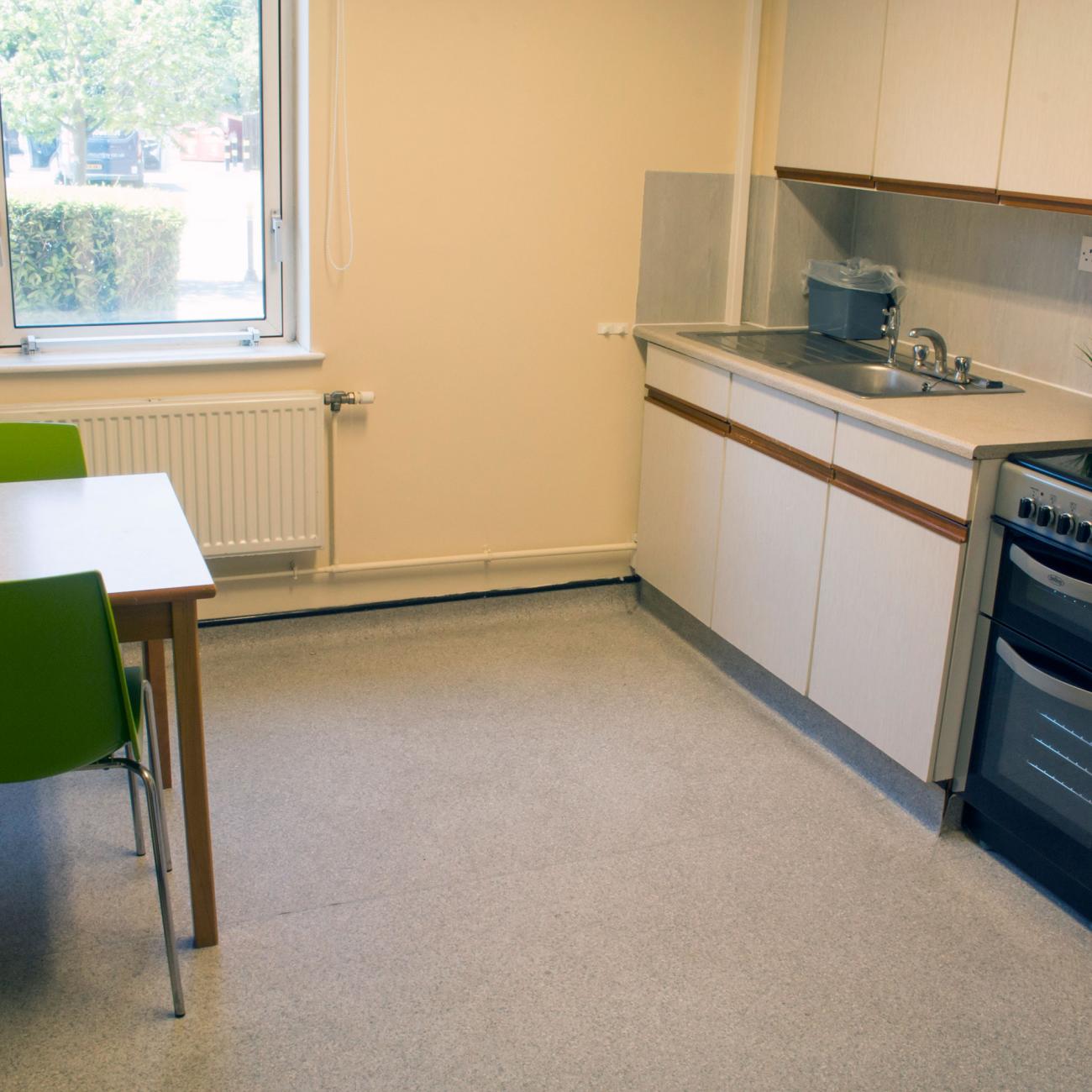A large kitchen with laminate flooring. It contains modern looking kitchen appliances and cupboards, a small square table with two chairs and a window.