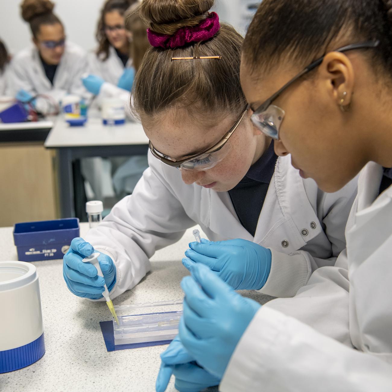 School pupils wearing goggles and gloves experimenting in lab
