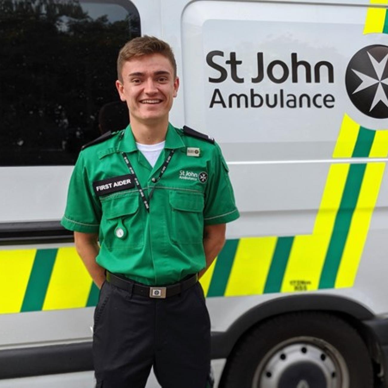 Thomas Edwards smiles as he stands next to an ambulance in his St John Ambulance uniform.