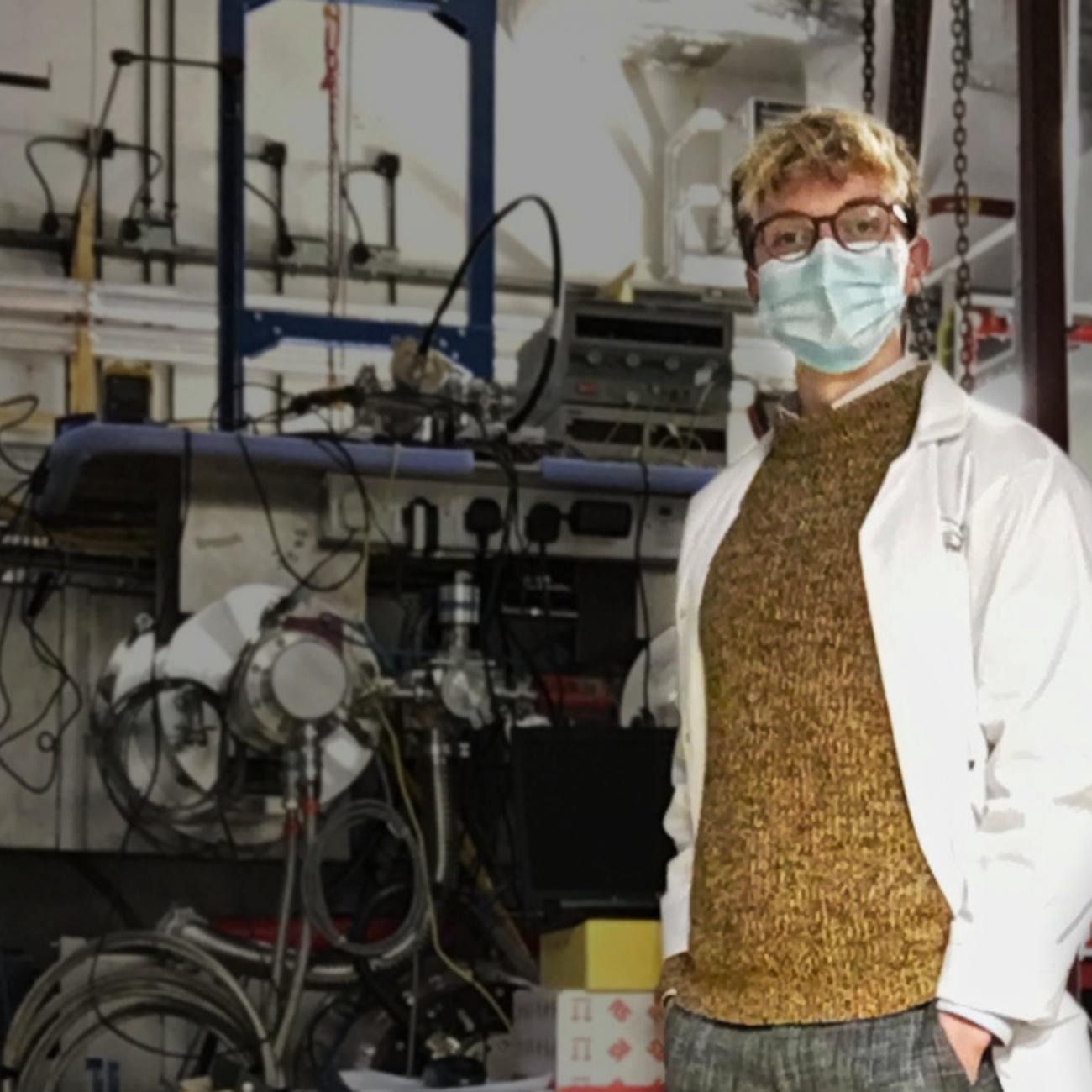 Engineering student Oliver Hitchens in a lab coat and mask in front of lab equipment