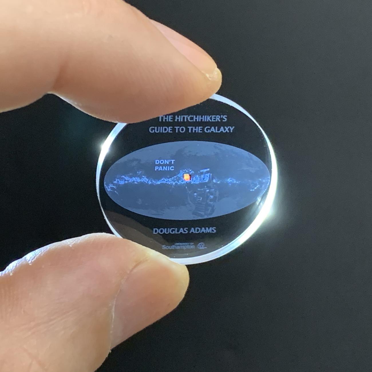 A 5-dimensional memory crystal imprinted with a copy of The Hitchhiker's Guide to the Galaxy by Douglas Adams. The crystal is pinched between two fingers, no larger than a coin.