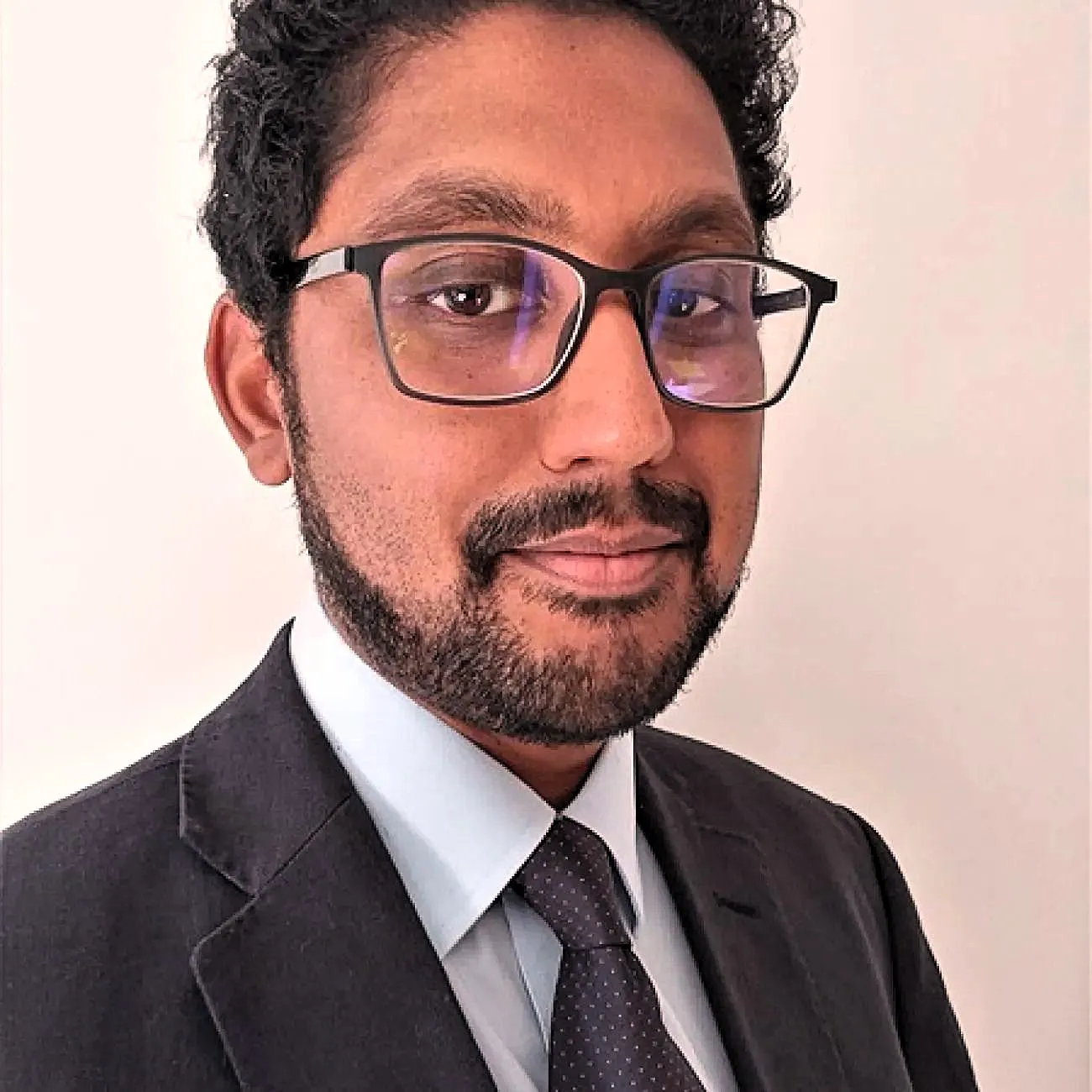 Dr Varatharaj looks out at the camera wearing a black suit and tie