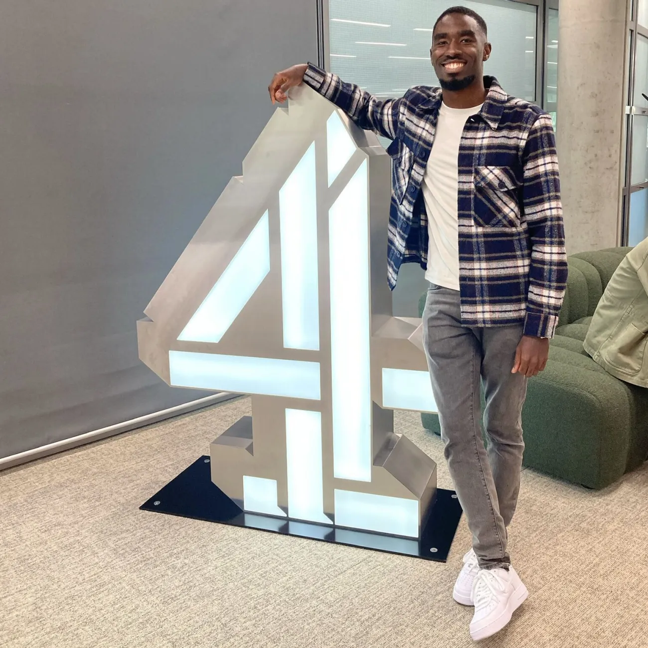 Samuel Ajayi standing next to a large Channel 4 logo.
