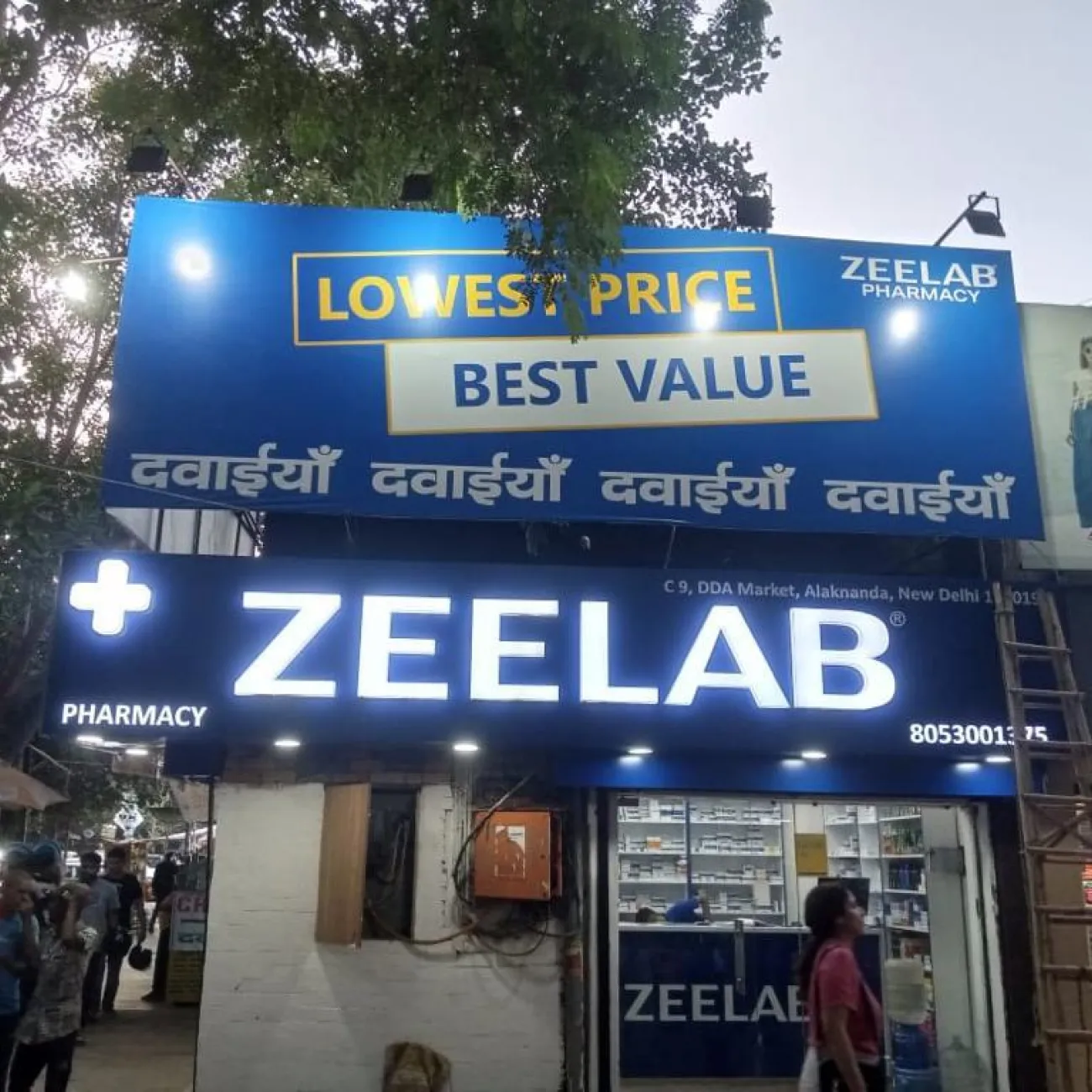 Rohit's pharmacy 'Zeelab' in Delhi. It has a large blue sign for 'Lowest price. Best value' and for the pharmacy name 'Zeelab'.