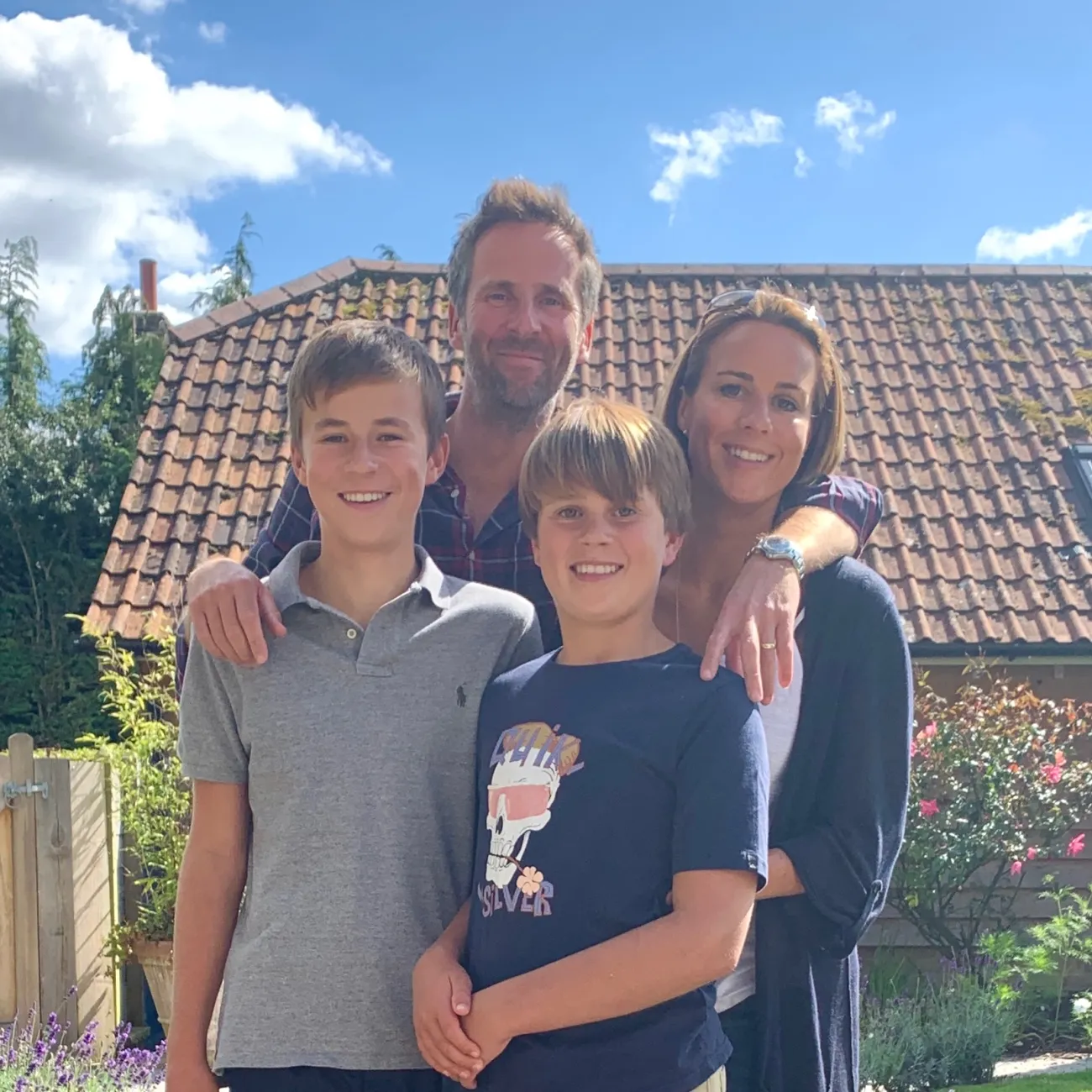 The Malpas family stood with their arms around each other, outside a typical British house with a sunny blue sky.