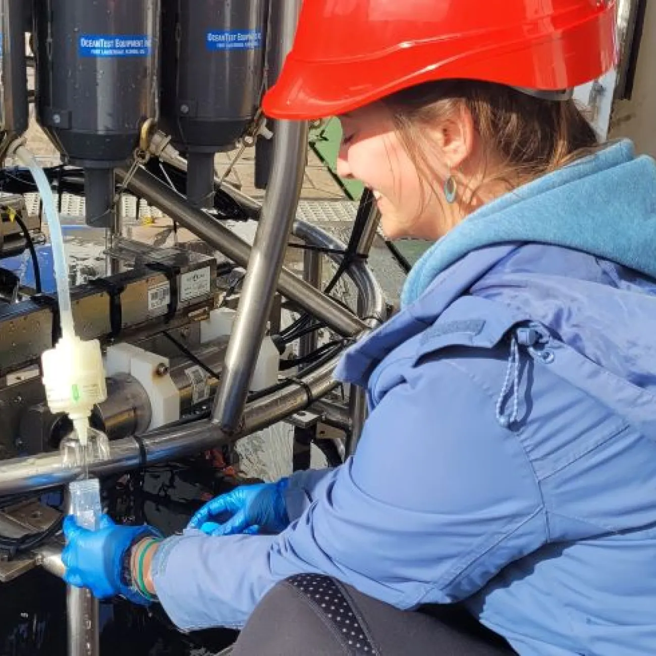 A researcher wearing a hard hat is collecting water samples on the Royal Research Ship Discovery.