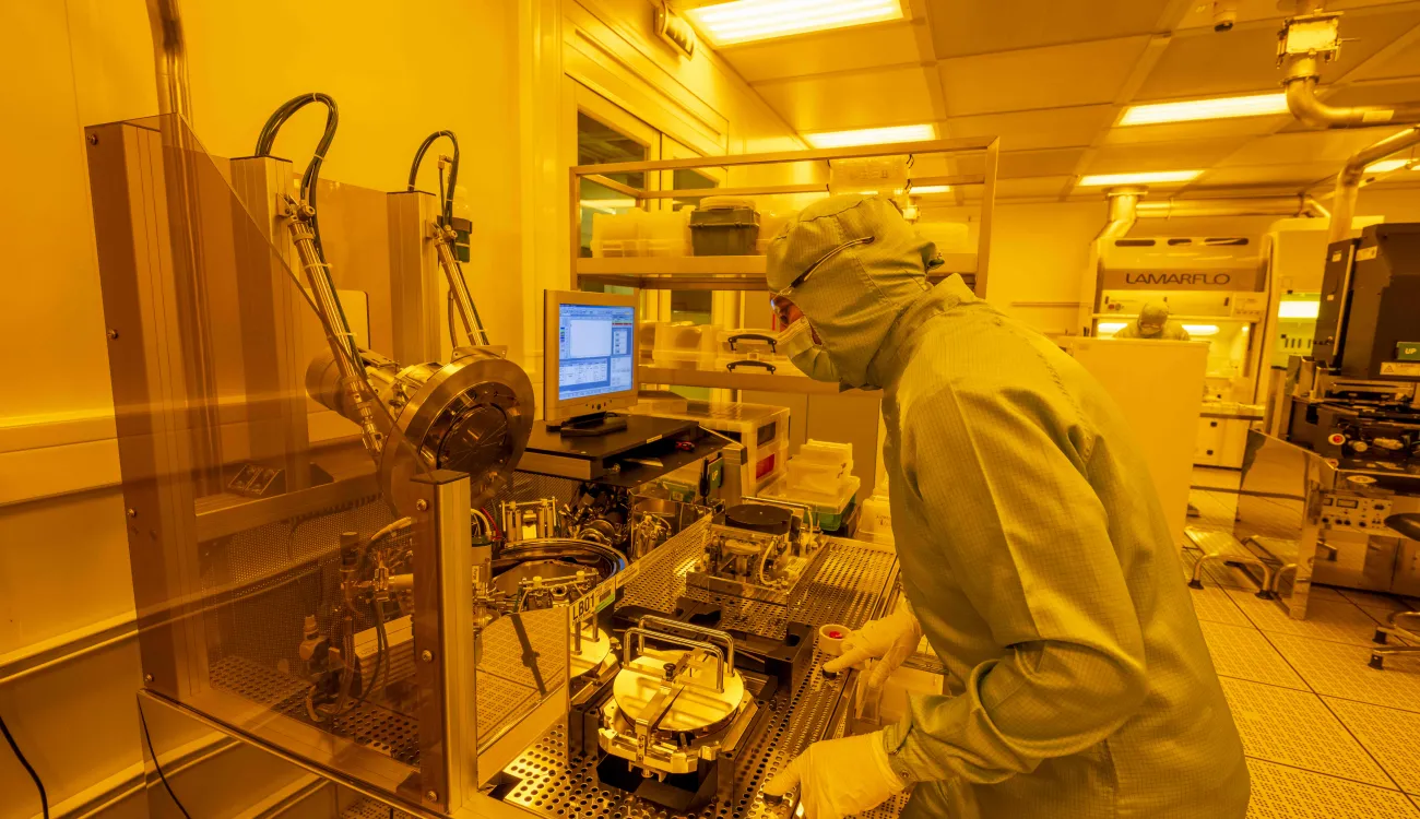 A researcher in a cleanroom suit uses the wafer bond tool