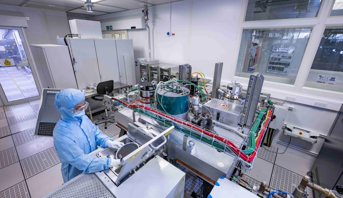 A researcher in cleanroom suit uses the Buhler Helios Batch Sputter Tool in the nanofabrication cleanroom
