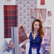 Textile design student with a collection of red and blue woven fabric samples at a course exhibition display.