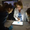 A lecturer and school pupils inspect a blue gel on a lightbox