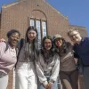Five postgraduate students stood smiling with their arms around each other outside Hartley Library on the University of Southampton's Highfield Campus. They are dressed in casual jumpers, shirts, and trousers.
